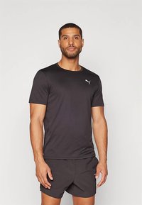 Camiseta desportiva preta de mangas curtas, feita de tecido suave, com um logotipo branco na área esquerda do peito, combinada com calções escuros.