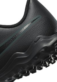 Scarpa sportiva nera con tomaia sintetica testurizzata, caratterizzata da dettagli verdi e un design della suola ondulato per una migliore aderenza. Nessun logo visibile.