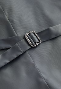 Gros plan d'une ceinture en tissu gris avec boucle métallique argentée sur un vêtement gris assorti avec des coutures visibles.