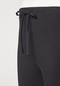 Svarta stretchjoggingbyxor med platt midjeband. Har dragsnörning och en slät, mjuk textur. Nära vy av midjebandets detalj.