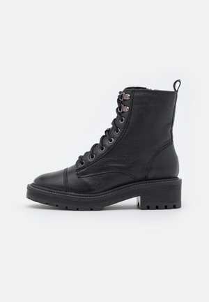 Bottine noire en cuir à lacets avec semelle épaisse, œillets en métal et languette de tirage à l'arrière, vue de profil sur fond blanc.