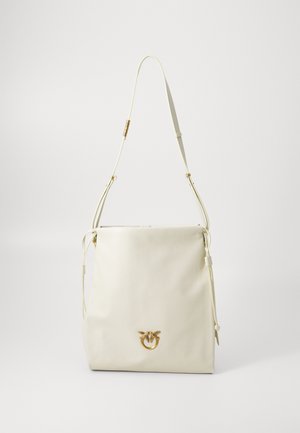 Krēma ādas plecu soma ar regulējamu siksnu un zelta putna formas aizdari uz vienkārša fona.