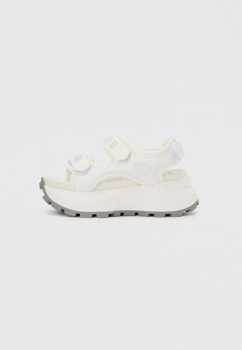 Λευκό πέδιλο πλατφόρμας με χοντρή γκρι σόλα με ανάγλυφο σχέδιο και ρυθμιζόμενους ιμάντες βέλκρο πάνω από τα δάχτυλα και τον αστράγαλο.