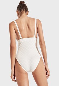 Bañador blanco de una sola pieza con finas tirantes ajustables, que presenta un patrón texturizado de círculos sutiles a lo largo de la tela.