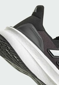 Svart och vit idrottssko med en texturerad ovandel, en tjock vit mellansula och en texturerad svart yttersula. "ULTRABOOST"-logotyp synlig.