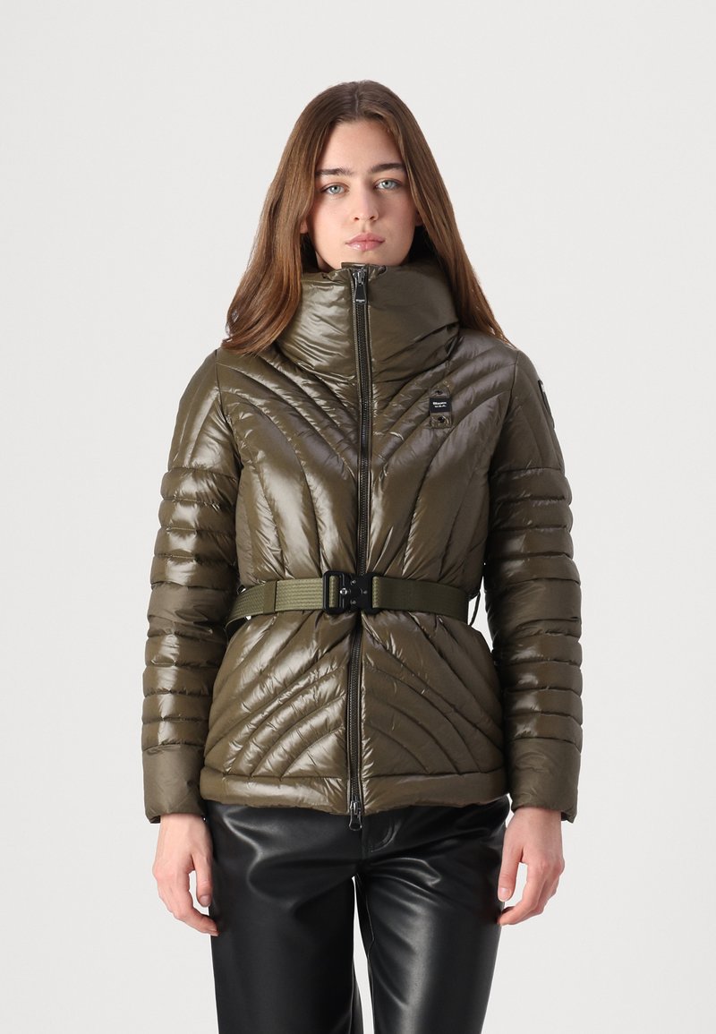 Olive green puffer jacket with a high collar, zip front, and belted waist. Features quilted design and glossy texture, paired with black pants.