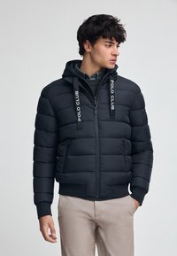 Czarna ocieplana kurtka z kapturem, z przodem na zamek błyskawiczny, elastycznymi mankietami i logo "POLO CLUB" na sznurkach. Gładka faktura.