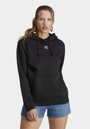Musta huppari, jossa on etutasku ja kiristysnauha hupussa, jossa on pieni valkoinen Adidasin trefoil-logo rinnassa. Yhdistettynä farkkushortseihin.