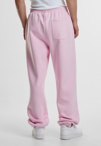 Lys rosa joggebukser med avslappet passform, elastisk midje og en enkel baklomme. Har ribbede mansjetter og en jevn, myk tekstur.