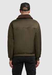 Jachetă bomber verde cu guler din blană sintetică maro, mansete și tiv elastic, și detalii cu buzunare laterale, prezentată din spate pe un fundal deschis.