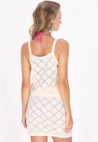 Top in crema con un design a rombi, caratterizzato da un orlo solido e un dettaglio in rosa legato al collo. Tessuto strutturato con una silhouette aderente.