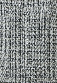 Textúrovaná tkanina s čierno-bielym houndstooth vzorom a metalickými zlatými akcentmi. Tkanie je husté s rôznymi hrúbkami nití.