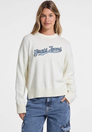 Maglione bianco a maglia con orlo e polsini a costine; presenta il logo ricamato blu "Guess Jeans" attraverso il petto; vestibilità ampia e design a girocollo.