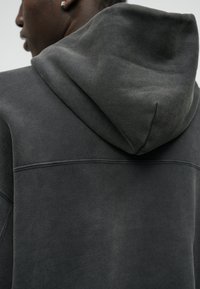 Sweatshirt à capuche gris avec une texture lisse, doté d'une capuche et d'un détail de couture contrasté au dos.