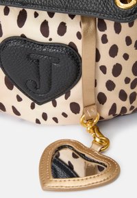 Borsa a forma di cuore in tessuto beige con macchie marroni, dettagli in pelle nera e una catena dorata con uno specchio a forma di cuore.