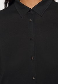 Svart skjorta med knappar och krage, med en slät yta och svarta knappar längs fram för stängning.