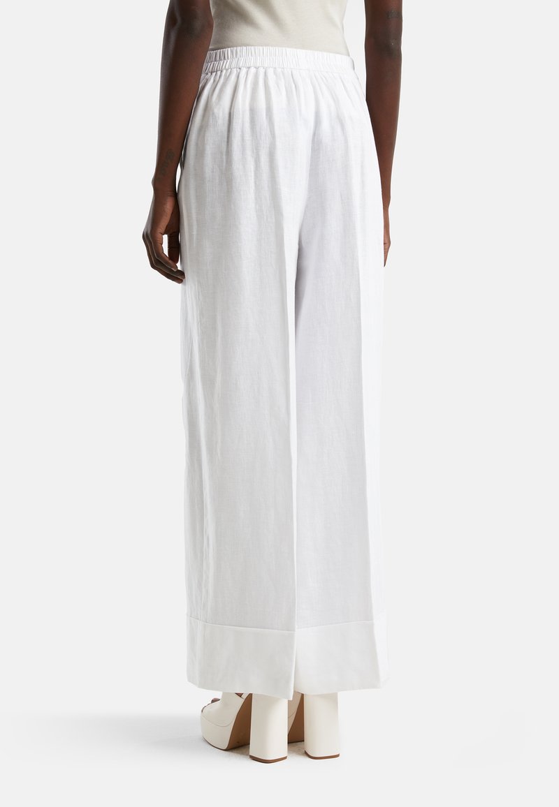 Białe lniane spodnie szerokie w nogawkach z elastycznym pasem, mające czysty brzeg i gładką fakturę. Noszone z jasnymi butami na niskim obcasie.