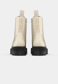 Botines color crema con un acabado brillante, que presentan una suela gruesa negra y la marca DKNY en las lengüetas traseras y en las cremalleras.