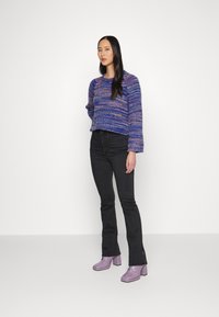 Suéter cropped tricotado em azul e roxo com mangas longas, combinado com jeans pretos wide leg e botas de salto lavanda.