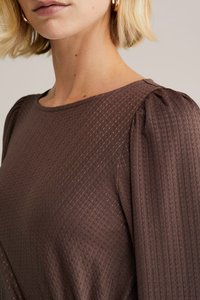 Brązowa, teksturowana bluzka z wzorem diamentowym, zaokrąglonym dekoltem i bufkami, wykonana z gładkiego materiału o subtelnym połysku.