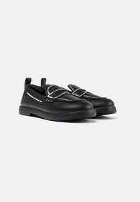 Scarpe slip-on nere con esterno in pelle liscia, cuciture bianche a contrasto e suole in gomma piatte; presentano linguette sul tallone per una facile calzata.