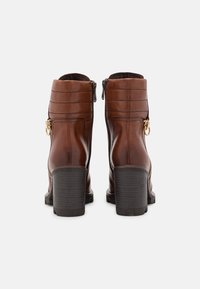 Bottines en cuir marron avec une finition texturée, des zips sur les côtés, des accessoires en métal doré, et des talons épais noirs. Couture renforcée sur la tige.
