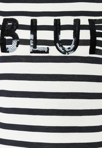 Textile T-shirt featuring horizontal black and white stripes, with large black and silver sequin letters spelling "BLUE" prominently displayed.