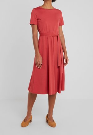 Rød kjole med korte ærmer, rund halsudskæring og bælte i taljen. Flowy nederdel, der går til midt på læggen. Bruges med vævede, brune hæle.