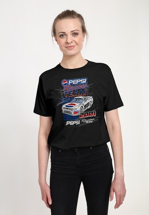 Kobieta nosząca czarną koszulkę z vintage grafiką Pepsi Racing Team i ilustracją samochodu wyścigowego na przodzie na jednolitym tle.