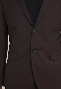 Bruine op maat gemaakte blazer met twee zwarte knopen, met een reverskraag en zijzakken, gemaakt van gladde stof met een subtiele glans.