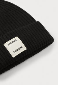 Black ribbed knit beanie with folded cuff featuring a white rectangular patch labeled "SAMSOE" twice in black text.