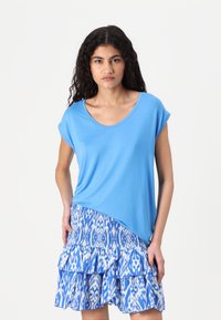 Blauw kortmouwtop met een ronde halslijn, gecombineerd met een blauw-witte rok met een patroon en ruffles. Zacht materiaal met een asymmetrische zoom.