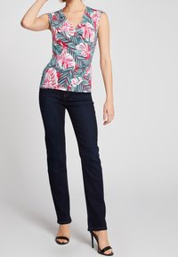 Ærmeløs top med v-hals og et tropisk blad mønster i pink og teal, parret med mørkeblå lige ben jeans og sorte højhælede sandaler.
