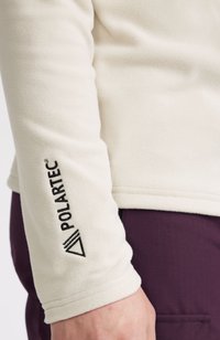 Pullover in pile beige con maniche lunghe e logo Polartec nero sul braccio sinistro. Tessuto liscio e polsini a coste.