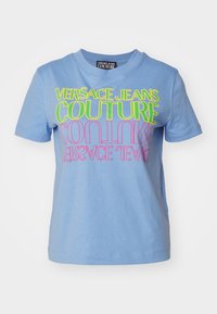 Světle modré bavlněné tričko s výrazným, barevným nápisem: "VERSACE JEANS COUTURE" v zelené a růžové. Krátké rukávy, kulatý výstřih, volný střih.