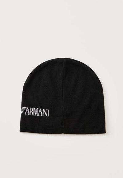 Bonnet en maille noir avec logo et emblème blanc Armani sur le bord inférieur, centré sur un fond gris clair uni.