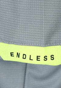 Tela gris con un patrón de cuadrícula, con un acento de color amarillo neón en la parte inferior que tiene el texto "ENDLESS" en negro.