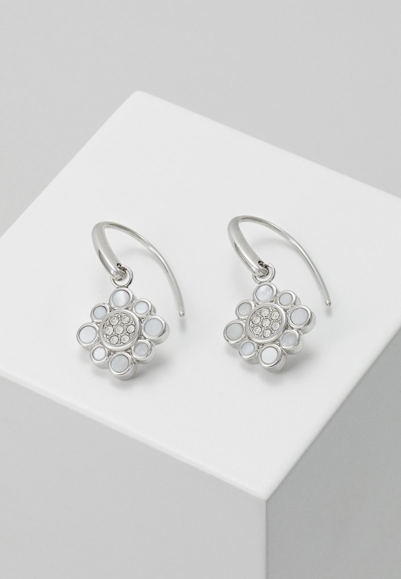 Boucles d'oreilles créoles florales en argent avec accents de cristal circulaires sur cube d'exposition blanc sur fond gris.