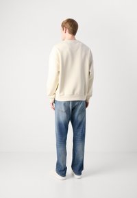 Kremfarget genser med avslappet passform, ribbede mansjetter og hem; sammen med falmet blå jeans og hvite sneakers, sett fra baksiden.