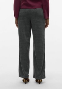 Grå rutiga byxor med vida ben och svarta och vita rutor. Tyget har en slät yta, kombinerat med bruna högklackade skor.