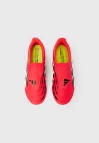 Ζευγάρι από λαμπερά κόκκινα ποδοσφαιρικά παπούτσια με μαύρες λεπτομέρειες και κίτρινες εσώσολες, σε λευκό φόντο και με θέα από πάνω.