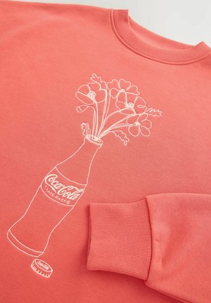 Koraalkleurige sweatshirt met een witte geborduurde afbeelding van een Coca-Cola-fles met bloemen. Ribbelkragen en -manchetten, zachte textuur.