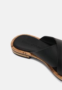 Sandale glissante en cuir noir avec un midsole en liège, présentant un design à lanières croisées. Texture lisse et marque discrète sur la semelle intérieure.