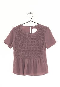 Blouse mauve à manches courtes avec un détail de smocking texturé sur la poitrine et un ourlet peplum ample. Ouverture en forme de clé à l'arrière. Étiquette de suspension visible.