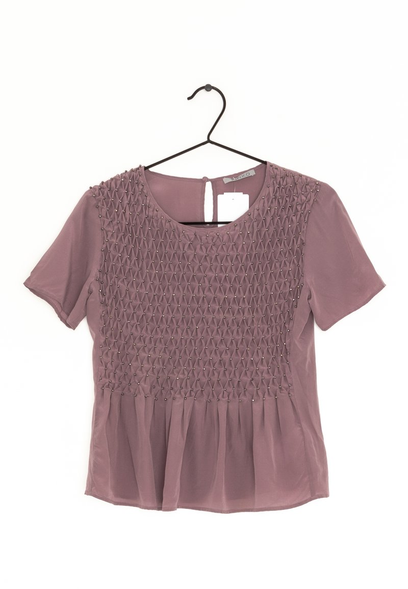Blouse mauve à manches courtes avec un détail de smocking texturé sur la poitrine et un ourlet peplum ample. Ouverture en forme de clé à l'arrière. Étiquette de suspension visible.