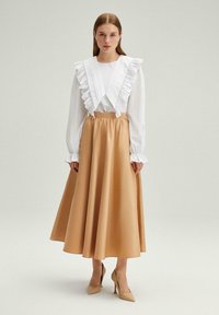 Blusa blanca con cuello y mangas con volantes, combinada con una falda midi de satén beige. El conjunto presenta un diseño fluido y una cintura ajustada.