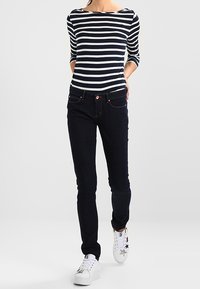 Parte superior de rayas azul marino y blanca de manga larga, jeans ajustados oscuros y zapatillas blancas con acentos de estrellas. Enfoque en una silueta casual y ajustada.