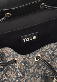 Borsa nera con un esterno beige testurizzato caratterizzato da un motivo astratto blu. Finiture dorate con lacci neri. All'interno è presente un'etichetta con il logo.
