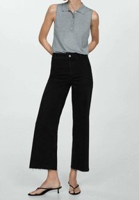 Camisa polo sin mangas gris con tres botones, combinada con unos vaqueros negros de pierna ancha de talle alto con dobladillos deshilachados, luciendo sandalias negras.