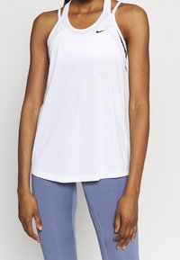 Woman wearing a white sleeveless Nike top and light blue fitted leggings, standing with arms relaxed by her sides.